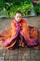 A woman sitting on a brick walkway wrapped in a blanket.