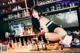 A woman sitting on top of a bar next to bottles of alcohol.